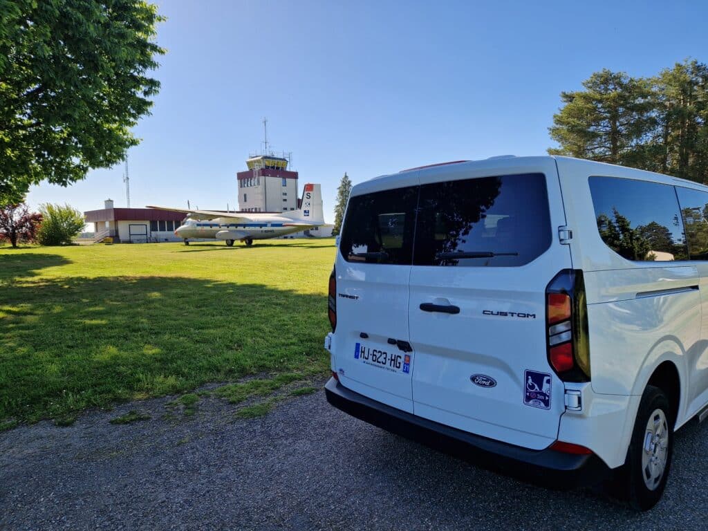 Ford Transit Custom blanc HJ-623-HG garé près d'un avion F-BPNS et d'une tour de contrôle par temps clair.