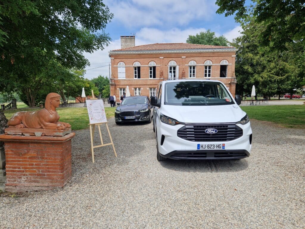 Véhicules Ford devant le domaine de Ronsac. Panneau : Bienvenue au mariage de Salma et Guillaume. Transport des invités a la cérémonie