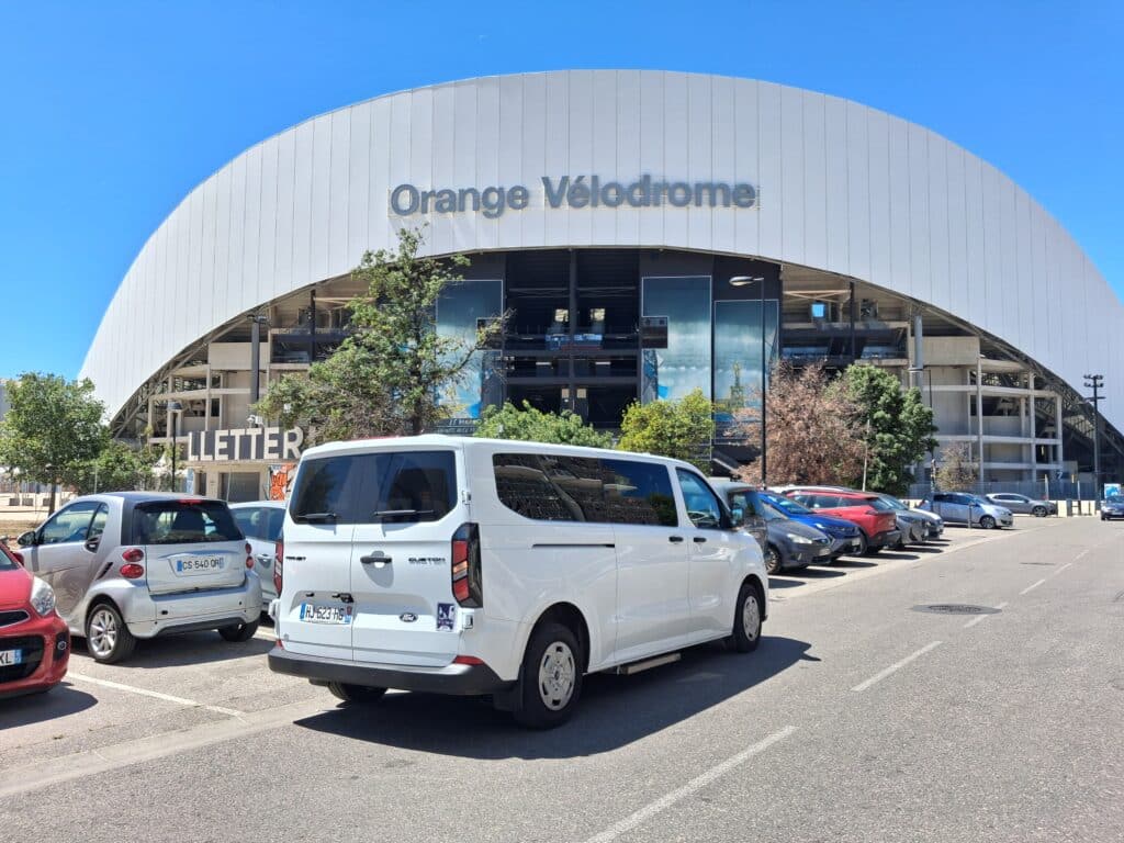 Stade Orange Vélodrome à Marseille avec voitures garées devant son dôme blanc sous un ciel bleu azur.