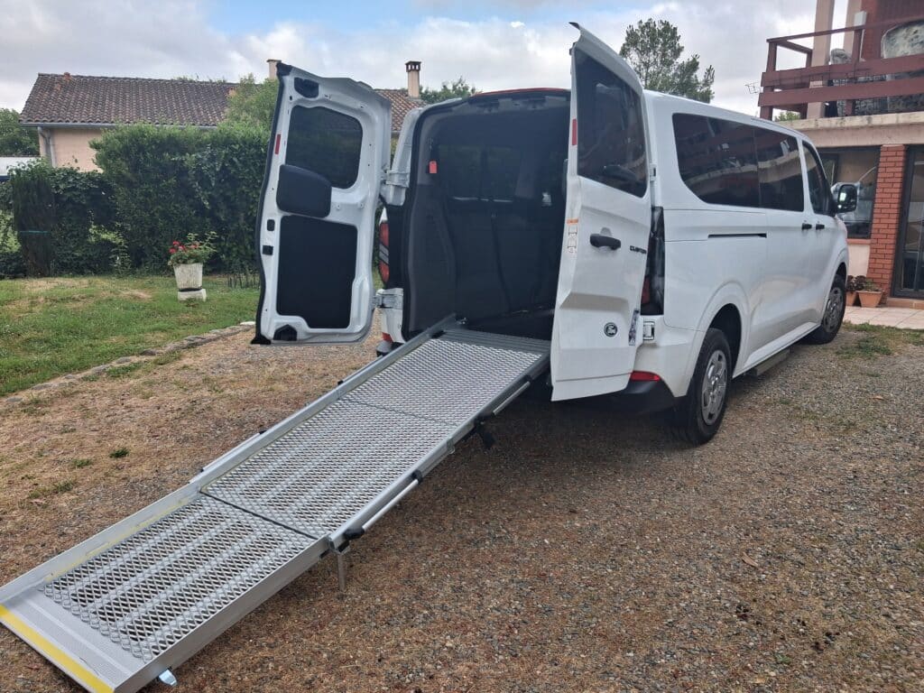 Van Ford blanc avec rampe PMR dépliée pour fauteuil roulant.