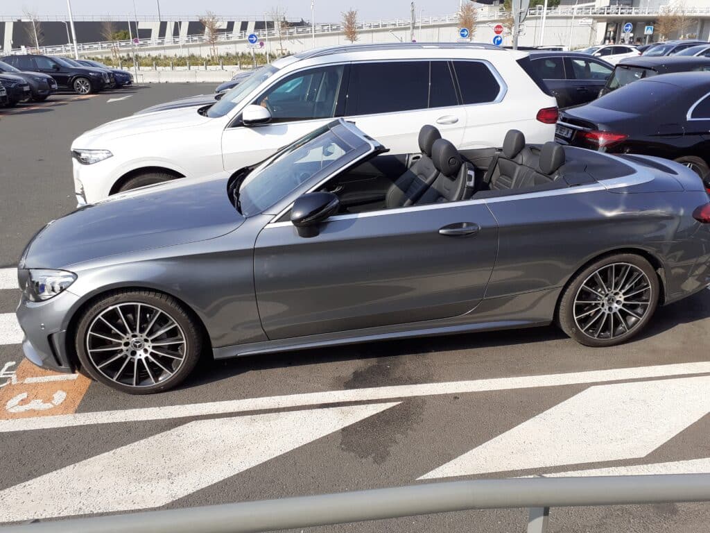 Mercedes-Benz décapotable grise stationnée sur un parking avec intérieur cuir noir et jantes sport.