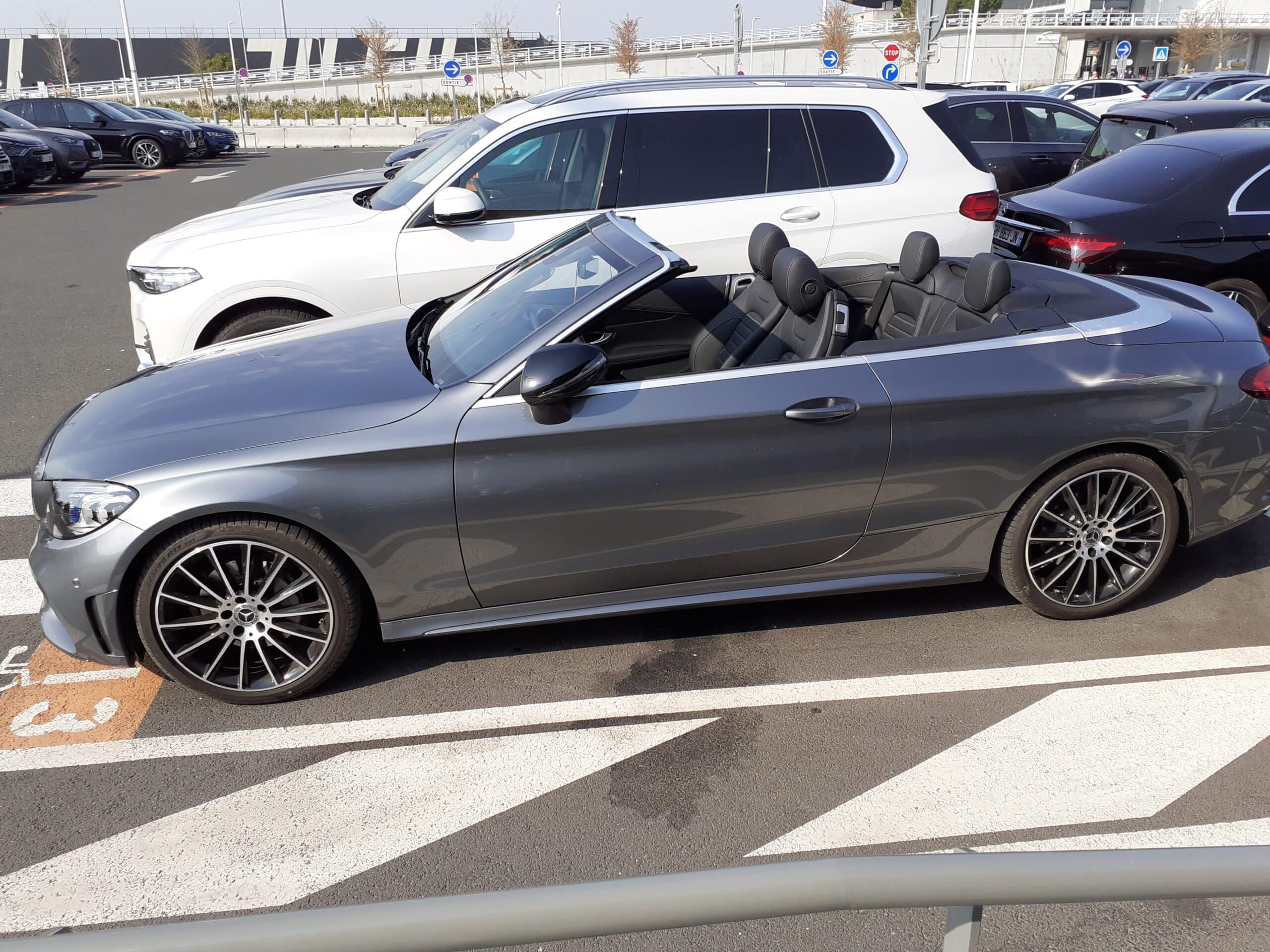 Mercedes Cabriolet Grise : Luxe et Performance en Parking Mercedes-Benz décapotable grise stationnée sur un parking avec intérieur cuir noir et jantes sport.